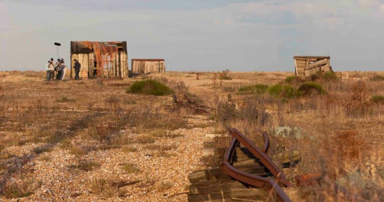 Vegetated shingle at Dungeness. Disused boat huts and camera crew on shingle